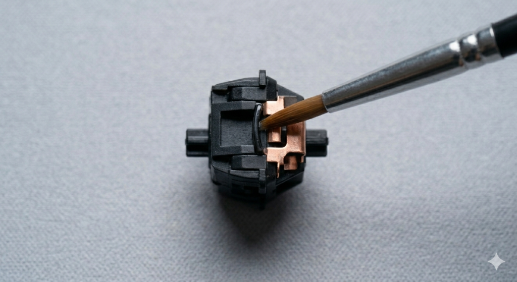 An extreme top-down macro view focused critically on a fine lubricating brush as it touches the vertical slide rail of a mechanical keyboard stem. The complex copper leaf contact within the switch is illuminated,